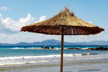Wicker, beach umbrella on a beautiful, empty beach overlooking the sea and mountains.