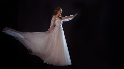 Young beautiful woman in wedding dress with wide light skirt. Dark background, fantasy style