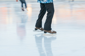 Cropped image of girl legs in brown old fashioned skates riding in the rink, in motion/ outdoor ice rink, selective focus on female, blurred background, frozen lake/ winter, sport and leisure concept.