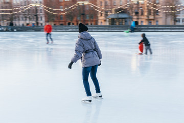 Cropped image of girl in white old fashioned skates riding backwards in the rink, in motion/ outdoor ice rink, selective focus on female, blurred background, frozen lake/winter and leisure concept