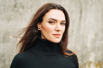 Outdoor portrait of young 35 year old woman with long dark hair, wearing black turtle neck dress