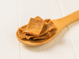 Crackers with herbs in a wooden spoon on a white wooden table. Selective focus.