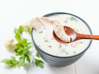 A piece of boiled chicken breast in a wooden spoon and cream cauliflower soup.