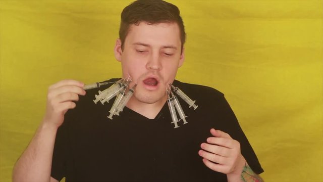 The man punctures his cheeks with syringes. emotional portrait of a crazy male in close-up. concept: the nervous breakdown, mental disease, headaches and migraine.
