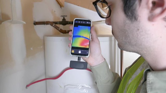 House inspector plumber using thermal imaging camera to check the warm water heater tank for any leaks or malfunctions.