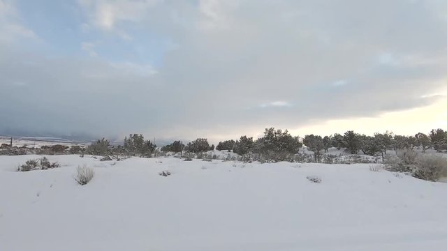 Drive Plate-POV-Side view passing snowy sage and juniper covered hill with setting sun under cloudy sky
