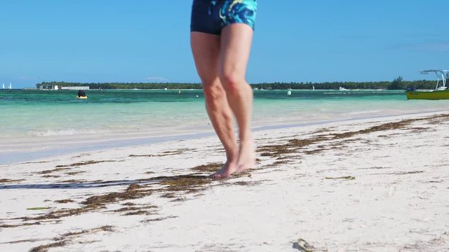 Unrecognizable man running along the beach. Closeup on legs at shore