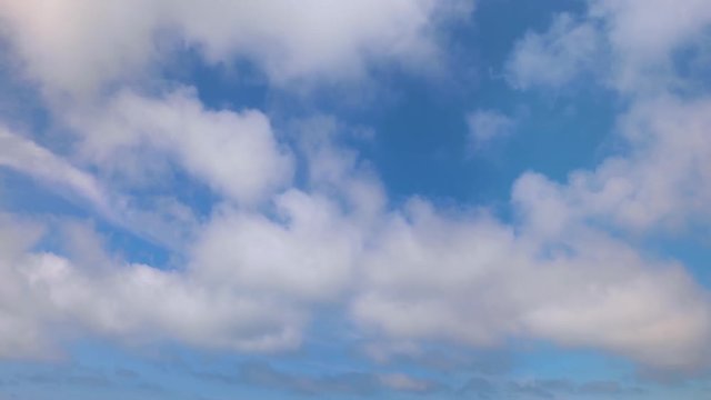 Looping one minute footage features white puffy clouds on a sunny day moving across a deep blue sky.