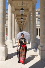 Fototapeta na wymiar Femme marchant avec une ombrelle sous un portique du palais royal
