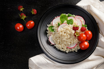 Quinoa salad with vegetables, raspberry and tomatoes on the black table. Super food for healthy and concept of balanced diet