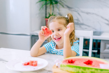 Happy baby girl eating watermelon in the kitchen. Baby food concept.