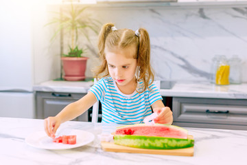 Happy baby girl eating watermelon in the kitchen. Baby food concept.