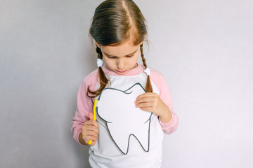 Cute girl holding toothbrush and tooth layout. Oral hygiene. Pediatric dentistry.