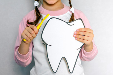 Cute girl holding toothbrush and tooth layout. Oral hygiene. Pediatric dentistry.