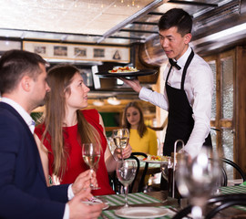 Frendly waiter is giving order for couple who is resting with white wine