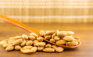 Almonds seeds pour from wood spoon on textured wooden background, top view.