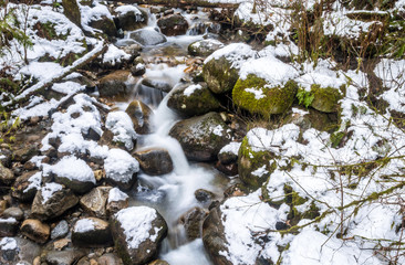 fresh water rushing down snow covered creek inside forest on a cold winter morning 