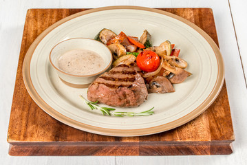 Steak with vegetables, mushrooms on a white plate with sauce