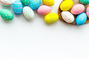Easter traditions. Colorful Easter eggs in basket on white background top view copy space border