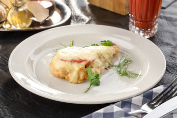Chicken breast fillet baked with Parmesan cheese, tomato and herbs with glass of tomato juice on the table