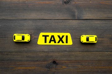 Taxi concept. Yellow service sign text taxi near car toy on dark wooden background top view copy...
