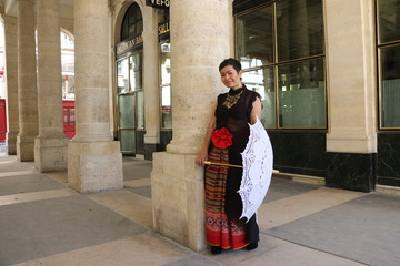 Fototapeta na wymiar Femme avec ombrelle blanche appuyée sur une colonne du palais royal à Paris