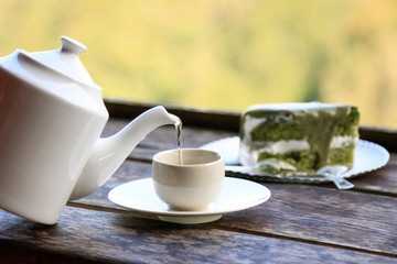 pouring hot tea from teapot with cake in cafe 