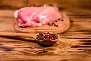 Cutting board with raw chicken fillet and spoon with different spices on wooden table
