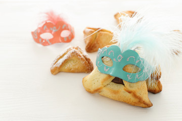 Obraz na płótnie Canvas Purim celebration concept (jewish carnival holiday). Traditional hamantaschen cookies with cute mask over white wooden table.