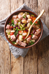 Portion of soup from beans, peas, ham, tomatoes and herbs close-up in a bowl. Vertical top view