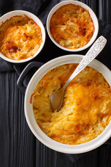potato gratin baked with sour cream, onions and cheddar cheese close-up in a pan. Vertical top view