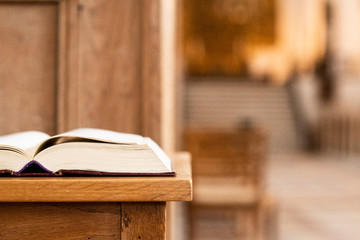 Holy book on a table in front of the altar of the church and with a view to the great big churchroom - obrazy, fototapety, plakaty