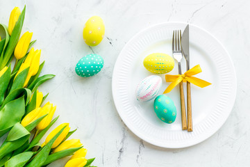Festive traditional Easter dinner concept. Tableware, painted eggs, tulips flowers on white stone...