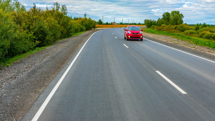 The red car goes on the road. New asphalt highway with fresh road markings