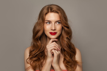Fototapeta premium Beautiful young red-haired woman with long beauty curly hair on brown background