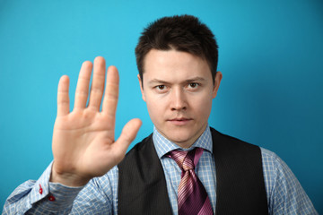 Young businessman in suit on blue background holds his hand in front of him, stop sign.