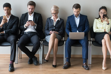 Diverse businesspeople sitting in row using devices phones and laptop