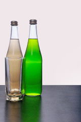 two bottles of refreshing lemonade and a glass with clear glass on a light background