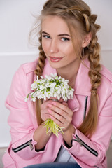 Beautiful woman with braided hair in a pink leather jacket with a bouquet of snowdrops. It's spring.