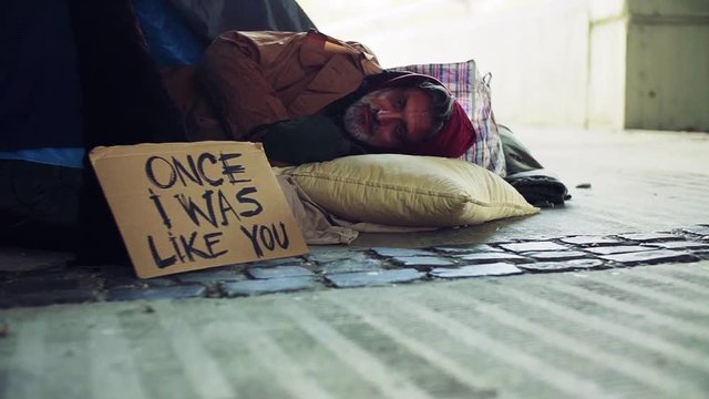 Homeless beggar man lying outdoors in a tent in city. Slow motion.