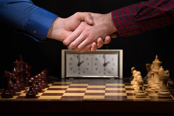 Handshake of businessmen before a game of chess close-up on a dark background and chess pieces