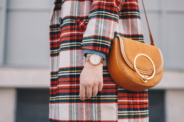 Close up of fashion details, stylish young fashion blogger wearing an overcoat with a tartan pattern and a wrist watch while holding a fancy yellow bag.