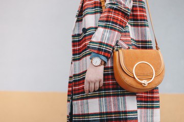 Close-up detail of stylish young woman wearing a coat with tartan pattern and a wrist watch while...