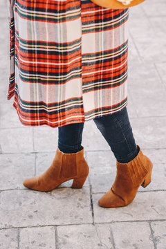 Fashion blogger outfit details. Fashionable woman wearing a plaid overcoat, black jeans and camel ankle shoes. Detail of a perfect fall or winter fashion outfit. Vertical image.