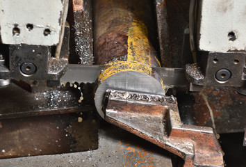 The process of cutting metal with an electric saw in a factory. Electric saw cuts round metal