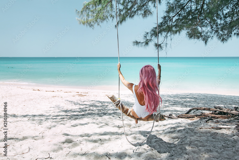 Wall mural girl with pink hair hanging on swing at beach