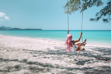 Fototapeta na wymiar Girl with pink hair hanging on swing at beach