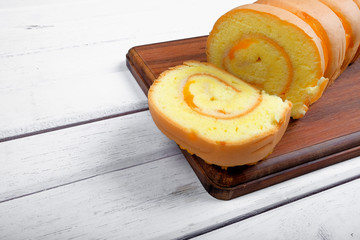 Roll cake  butter cream filling and on wooden plate over white wooden background