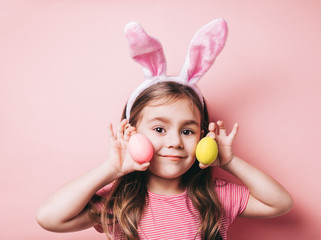 Easter girl portrait. Cute little girl with bunny ears on pink background. Easter child portrait, funny emotions, surprise. Copyspace for text.