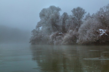 River in the fog. Forest by the river in hoarfrost, hoarfrost. Background water of the river and the forest on the shore in the fog.
